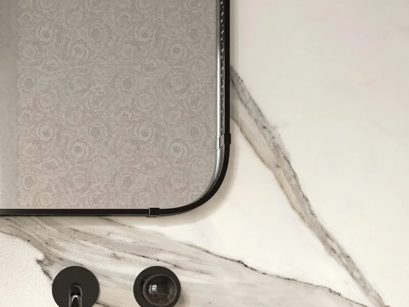 Corner of a Greek mirror in black nickel, Greek key running along the frame, against pale marble