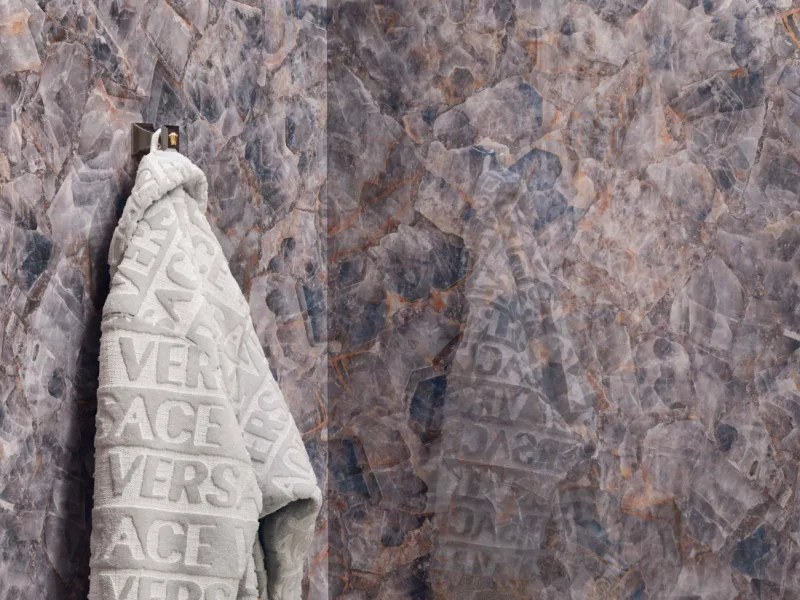 A Versace towel on a Superbe hook against a brown marble wall